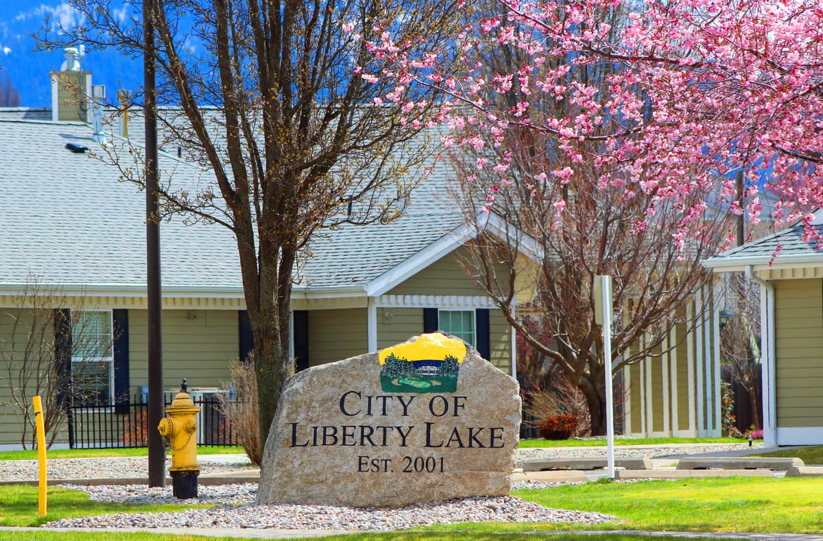 A stone sign reading "City of Liberty Lake, Est. 2001" under a blossoming cherry tree